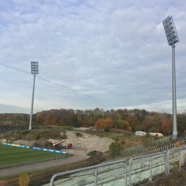 Blick von den Resten der überwucherten Tribüne des Parkstadions. Im Hintergrund schüttet ein LKW Material auf.